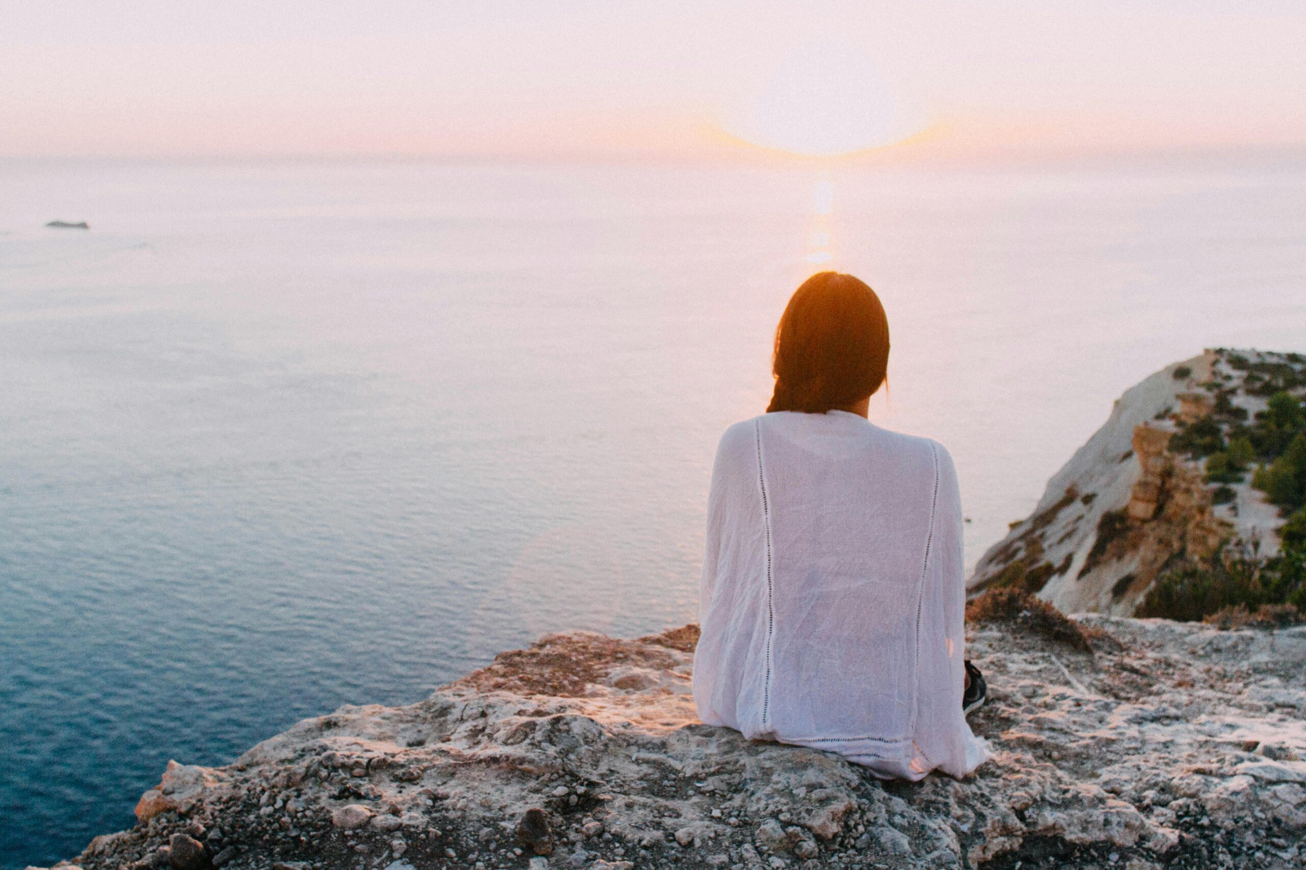 Woman on a cliff overlooking the ocean and the sunset onthe horizon