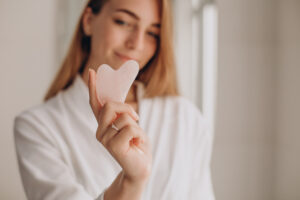 Woman performing self care with a spa robe on and a facial tool in hand